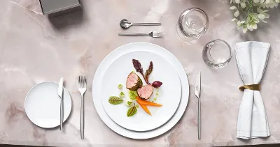 Stylish marble table with gourmet food on white MetroChic plates, together with MetroChic cutlery and floral decorations.