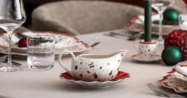 A festive table setting with Villeroy & Boch Toy’s Delight Christmas crockery including a gravy boat, together with wine glasses and a lit candle.