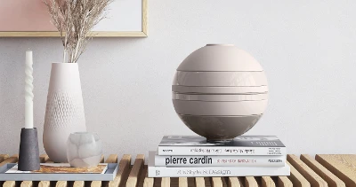 A beige La Boule from Villeroy & Boch on a wooden table next to a vase and books.