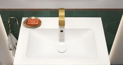 Waschbeckenbereich im Badezimmer mit goldenem Wasserhahn, weißem Waschbecken und einer Seifenschale mit einem roten Seifenstück. Der Waschbeckenschrank hat eine Holzoberfläche und der Boden ist mit sechseckigen Formen in Grün, Rosa und Weiß gefliest.