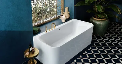 Ein luxuriöses Badezimmer mit einer  Vorwand-Badewanne aus der Loop & Friends Kollektion von Villeroy & Boch. Die Wanne ist weiß und hat goldene Armaturen. Das Bad ist in tiefem Blau gehalten, mit gemusterten Fliesen am Boden.