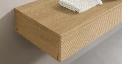 Een houten wastafel van Villeroy & Boch met een gestructureerde voorkant, waarop een witte handdoek en toiletartikelen liggen.