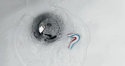 Dirty washbasin with flowing water A small amount of toothpaste and water is flowing down the drain of a bathroom washbasin, causing bubbles to form around the drain cover.
