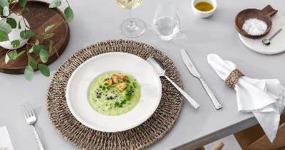 A dining table with Blacksmith flatware, an Artesano dish filled with soup, a glass of white wine and rustic table decorations.