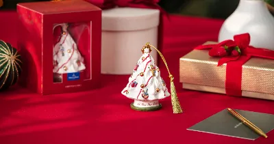 Porcelain Christmas tree ornaments on a red table, near a gift box, packaging, and a pen with Christmas decorations.