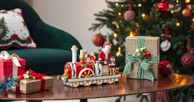  decorated Christmas tree, presents, and a Christmas Toys Memory locomotive on a wooden table next to a green chair.