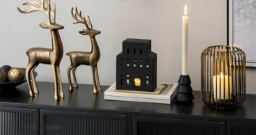 Two metal reindeer, candle holders and a black, house-shaped lantern on a black sideboard.