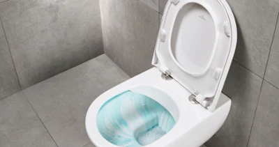 Wall-mounted toilet in white A wall-mounted toilet with flush technology from Villeroy & Boch against a grey tiled background. The toilet lid is open to reveal the bowl which contains a cleaning solution.