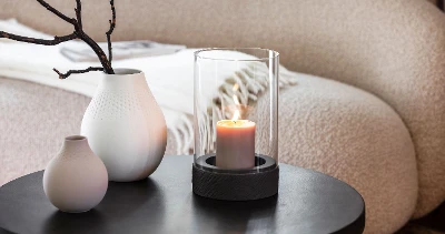 A Manufacture candle stands on a table next to two Manufacture vases.