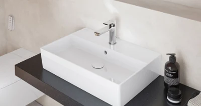 Single washbasin in White Alpin on dark countertop Minimalist Memento 2.0 single washbasin in glossy white, set on a dark countertop with modern chrome tap for a stylish bathroom look.