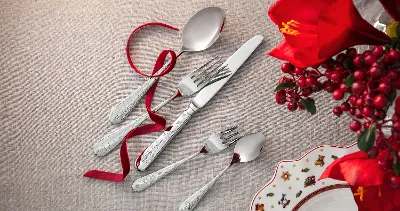 A Toy’s Delight flatware set consisting of a spoon, fork, knife, and two small spoons, arranged on a beige cloth with a red bow.