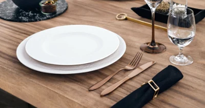 A bronze cutlery set lies next to a white plate on a wooden table.