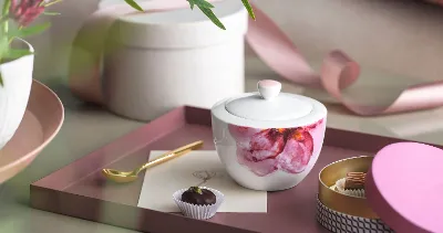 A Rose Garden sugar bowl with a candle, a gold spoon, a chocolate truffle and decorative items on a tray.