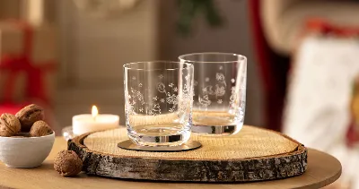 Two Toy’s Delight glasses on a wooden disk with a candle and a bowl of walnuts on a table.