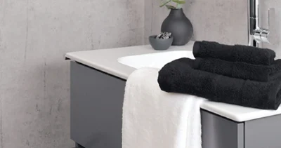 Un lavabo gris moderne de la collection « Finion » de Villeroy & Boch, avec des serviettes « One » blanches et noires. En arrière-plan se trouve un vase noir de la collection « Manufacture Collier » de Villeroy & Boch.