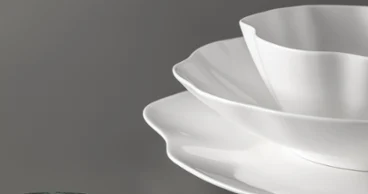 Trois assiettes blanches Pura à bord dentelé sont empilées sur une surface grise à côté d'un objet rond vert.