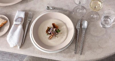 Ein gedeckter Tisch mit NewMoon Tellern und Besteck von Villeroy & Boch mit Cremesuppe.