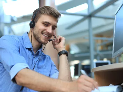 Lächelnder Mann mit Headset, der in einer Büroumgebung an einem Computer arbeitet.