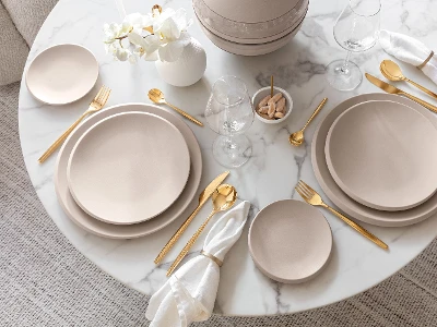 Een gedekte tafel met beige NewMoon borden en gouden MetroChic bestek van Villeroy & Boch.