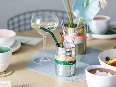 Elegant dining table setting with a glass of white wine, colourful straws in a decorative holder and bowls of fresh fruit and smoothies.