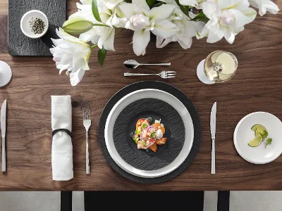Décoration de table élégante avec un plat de fruits de mer sur des assiettes Manufacture, des fleurs blanches, un verre de vin blanc et une petite assiette avec des tranches de citron.