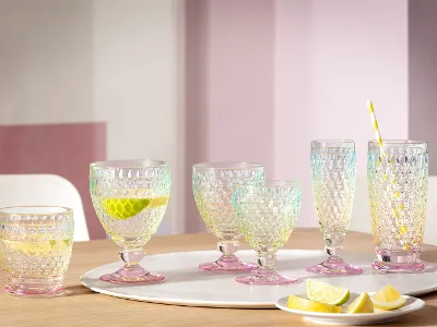 Ein Set aus sechs Villeroy & Boch Boston Pearl-Glasbechern auf einem Holztisch mit Limetten- und Zitronenscheiben, ein Becher mit Strohhalm und Zitronenscheibe.