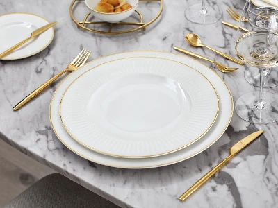 A white and gold dinnerware set from Château Septfontaines on a marble table.