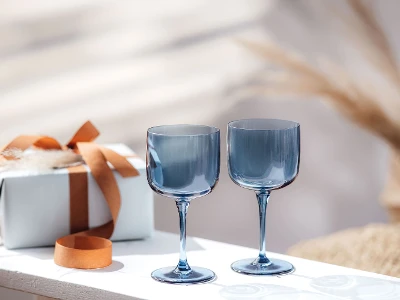 Two blue like. wine glasses on a table next to a gift box.