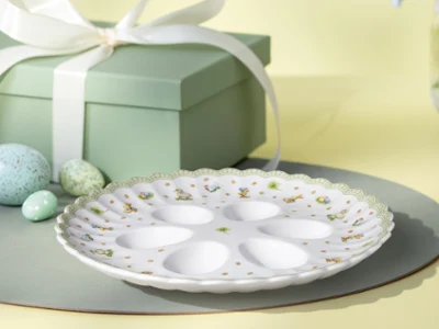 Decorative Easter Delight egg plate with eight sections sits on a placemat next to pastel eggs and a green gift box with a white ribbon.