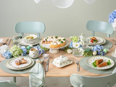 A Easter Delight dining table set for four with Easter Delight decorations, pastel tableware, and plates of food arranged neatly.