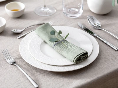 A set table with two white Manufacture plates, pastel green napkin, Piemont flatware and eucalyptus.