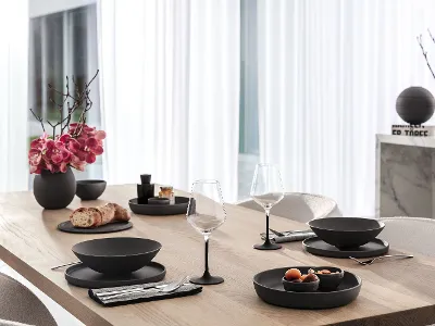 Un tavolo da pranzo in legno apparecchiato con una La Boule nera, bicchieri Manufacture e posate Piemont di Villeroy & Boch.