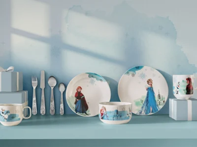 Stoviglie e utensili per bambini con personaggi di Frozen, esposti con scatole regalo blu su uno scaffale blu.