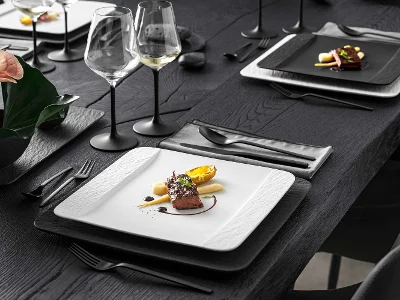 Manufacture dinnerware in black and white with main course served on black table. Next to it are glasses with black stem from Villeroy & Boch.