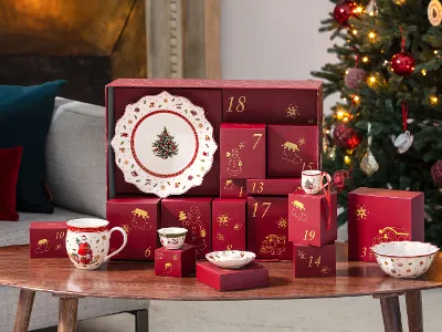 Rote Adventskalenderschachteln und weihnachtliches Geschirr stehen auf einem Holztisch neben einem geschmückten Weihnachtsbaum.
