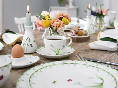 Elegante tafeldecoratie met Colourful Spring servies met bloemmotieven, verse bloemen en brandende kaarsen voor een verfijnde maaltijd.