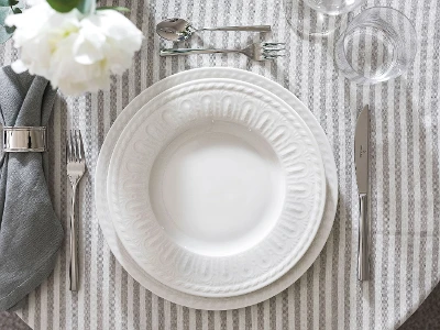 Elegant table decoration with white, embossed Cellini plate, flatware and folded gray napkin.