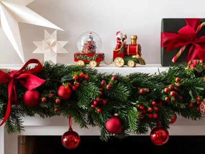 Une cheminée décorée de manière festive avec le train décoratif de la collection Christmas Toy Un manteau de cheminée décoré de manière festive avec le train décoratif de la collection Christmas Toy-collection de Villeroy & Boch. Avec les ornements rouges d'une boule à neige, des décorations en forme d'étoile et une boîte cadeau verte ornée d'un ruban rouge et d'un bâton de sucre.