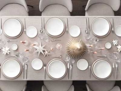 NewMoon and NewMoon Beige – A Natural Christmas Setting for Six Vista cenital de una mesa festiva para seis personas con las colecciones NewMoon y NewMoon Beige de Villeroy & Boch: platos de cena, cuencos planos, platos de pan y cuencos para salsas. Acompañada de copas de vino NewMoon, vasos y un juego de cubiertos de 30 piezas. La mesa está decorada con adornos navideños minimalistas — estrellas blancas y árboles de Navidad de madera — creando un ambiente cálido, natural y elegante.