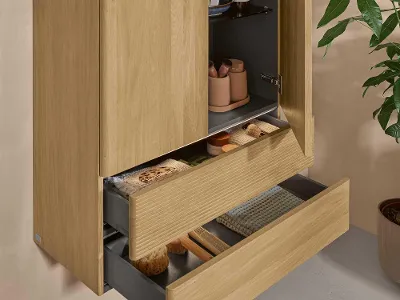 Ein Badschrank aus hellem Holz mit zwei Türen und zwei offenen Schubladen von Villeroy & Boch an einer naturbelassenen Wand.