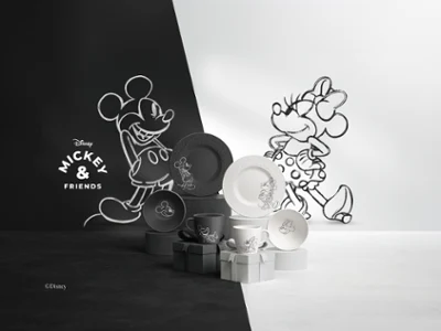 Una serie di piatti e tazze bianchi e neri della collezione Manufacture Mickey, disposti su una superficie divisa in due metà bianca e nera.