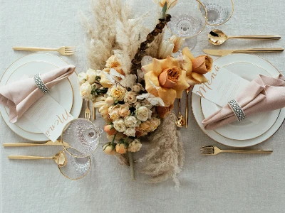 Elegante tafeldecoratie met goudkleurig MetroChic bestek, Anmut servies met gouden rand, floraal center piece en menukaarten.