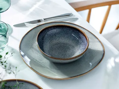 Une table dressée pour l’été avec de la vaisselle en grès artisanale Lave Beige à l’émail réactif, accompagnée de verres translucides en bleu clair pour une élégance naturelle.