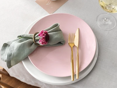 A set table with a pink Rose Garden plate, white NewMoon plate and gold MetroChic flatware.