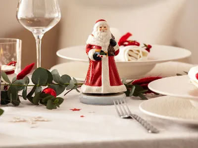 A festive table setting with a Nostaligic Melody Father Christmas music box in the centre, surrounded by plates, glasses, cutlery and green plants.