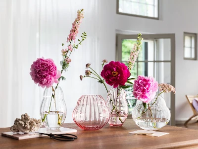 Four different vases from the Rose Garden collection by Villeroy & Boch stand on a wooden table.