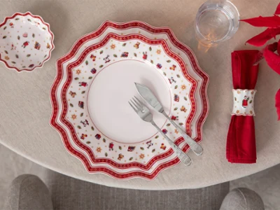 A festively laid table with red-and-white patterned crockery, a red napkin, and a knife and fork on a round table.