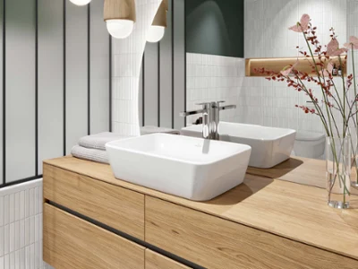 Une salle de bains moderne avec une vasque à poser Architectura blanche, des lampes suspendues décoratives, un miroir incurvé et un vase avec des fleurs séchées.