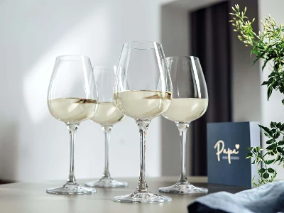 Drei Gläser Weißwein aus der Kollektion Purismo auf einem Tisch mit Grußkarte im Hintergrund.