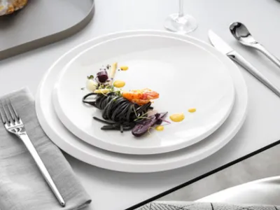 Ein elegantes Tischarrangement mit weißen Tellern und Speisen aus der NewMoon Kollektion, stilvoll arrangiert mit Besteck.

